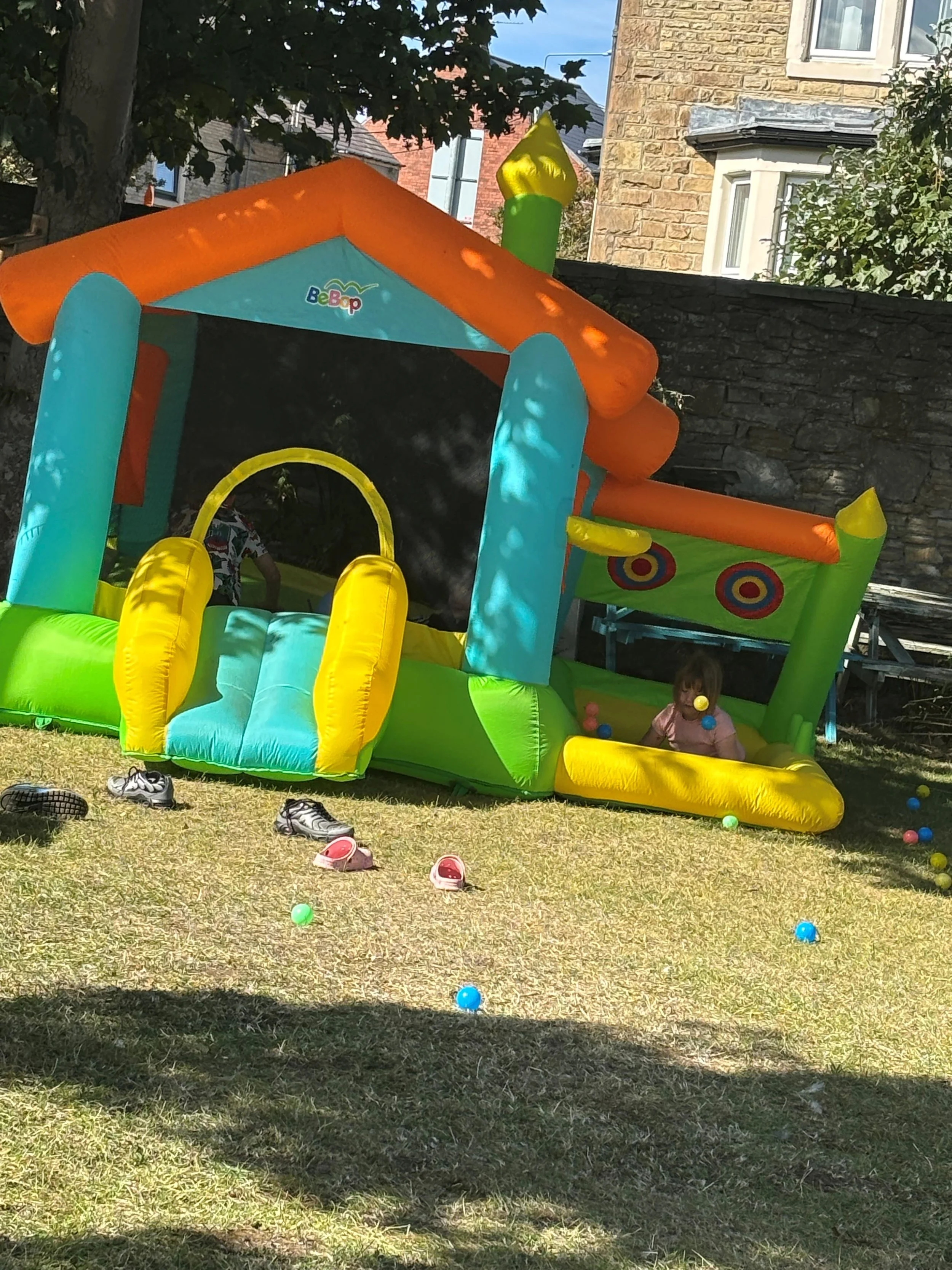 Colorful inflatable bounce house with a slide, children playing inside, and scattered colorful balls on the grass outside.