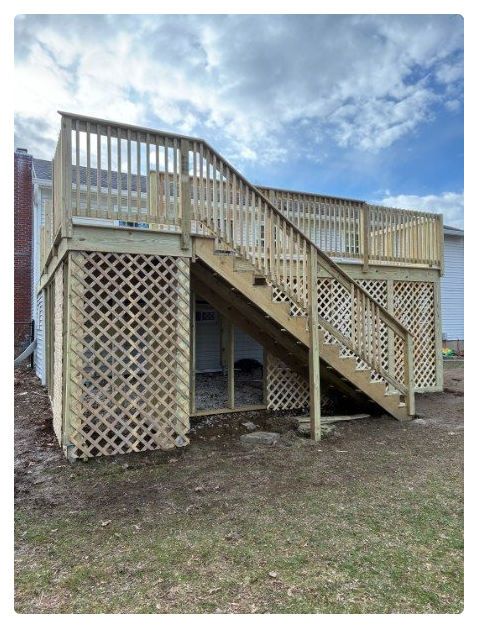 Wooden outdoor staircase with a railing, leading to a second-story deck on a house, with lattice panels underneath.