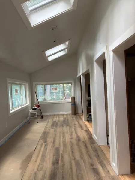 An unfinished room with new wood flooring, white walls, multiple windows, and skylights in the ceiling.
