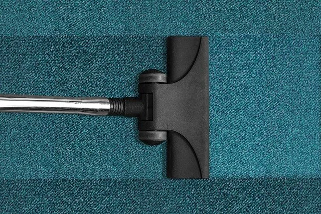 Vacuum cleaner nozzle cleaning a teal carpet.