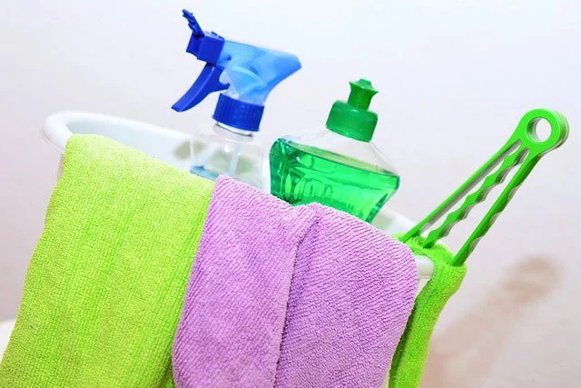 Cleaning supplies including spray bottles, green dish soap, green and purple towels, and a green scrub brush.