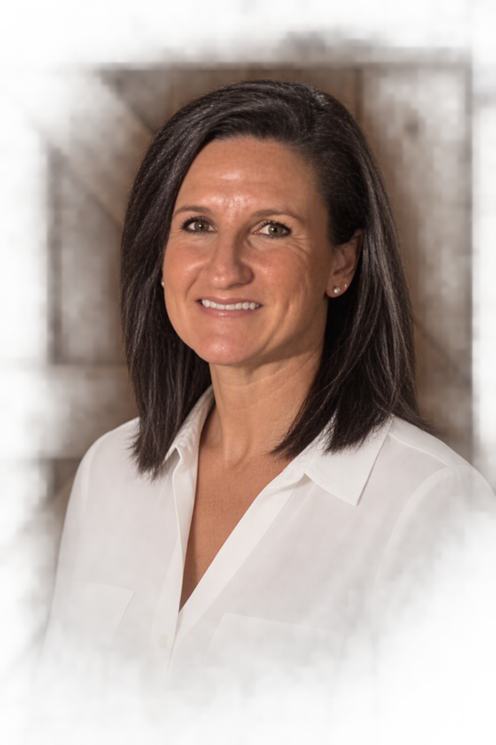 A woman with dark brown hair, wearing a white collared shirt, smiling, standing against a wooden background.