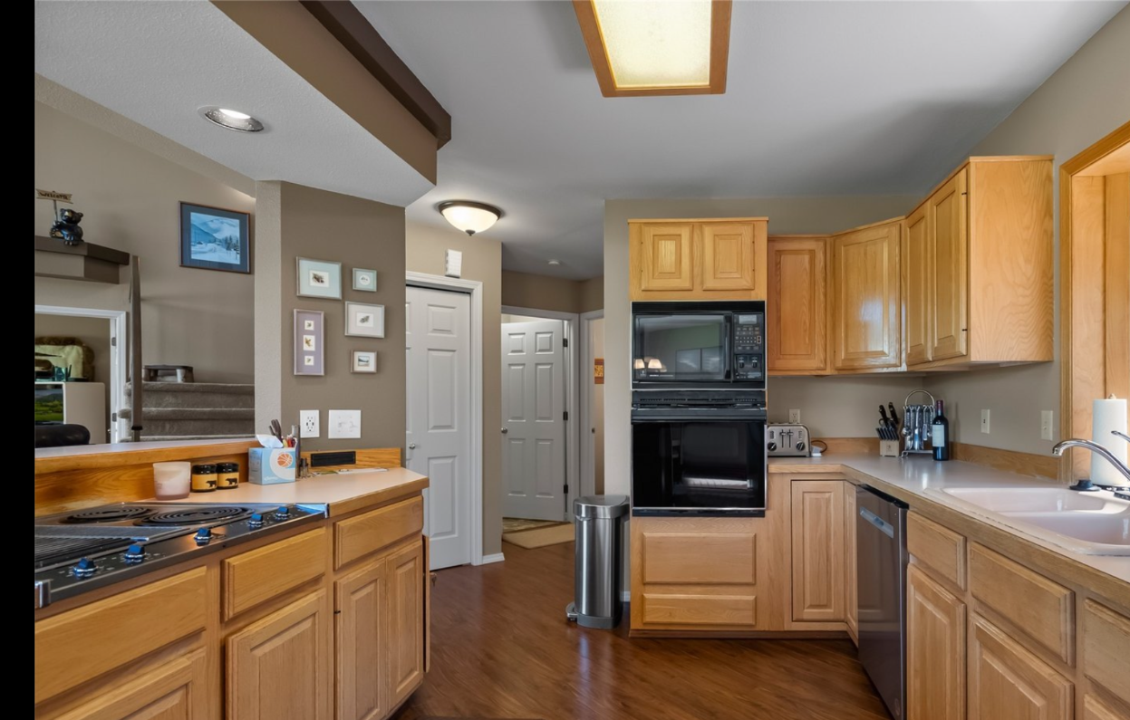 Kitchen with wooden cabinets, black appliances including microwave and oven, stainless steel trash can, dishwasher, and sink, with tan walls and hardwood floors.