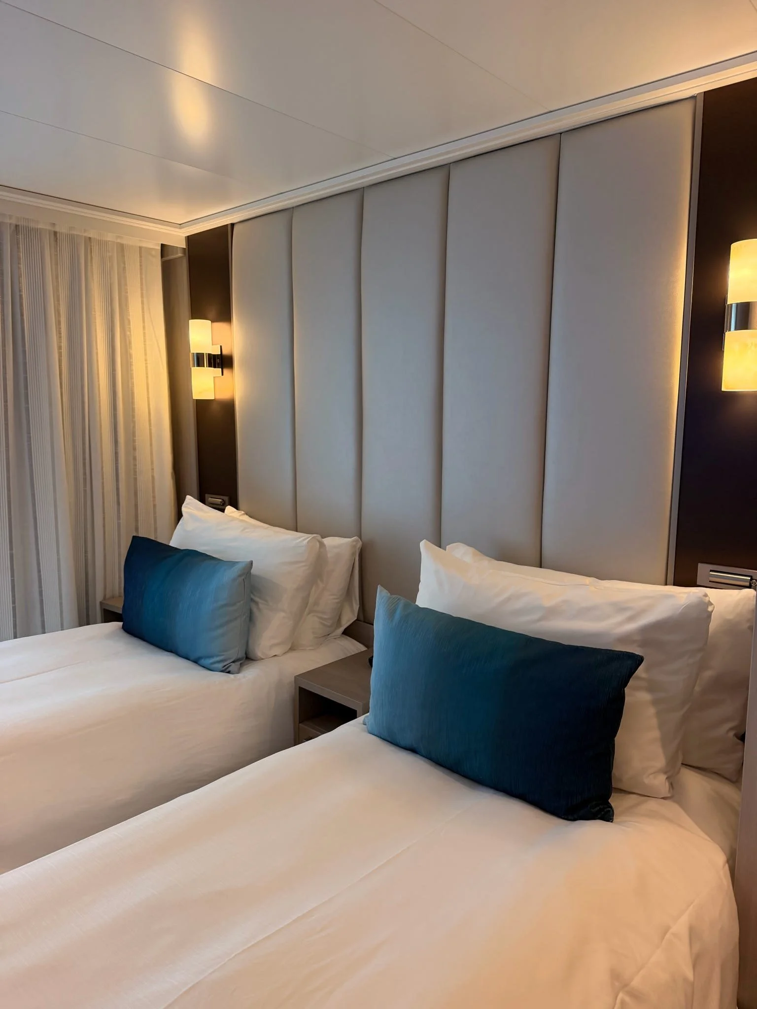 Two neatly made beds Star Princess highlighting the furniture that is perfect for travelers, especially those traveling with a CPAP due to large nightstand and electrical plugs by the bed.