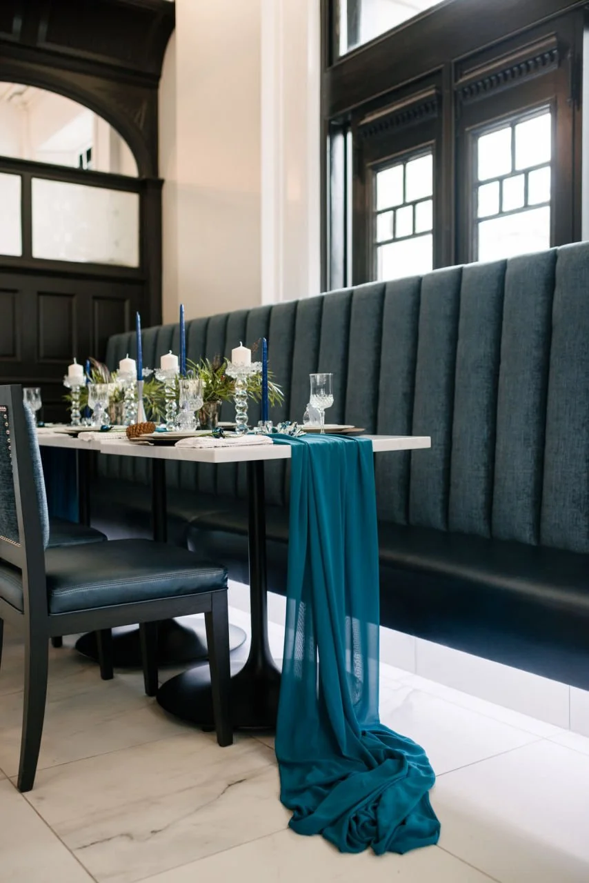 Blue pholstered benches, white tables with winter tablescape decor including winter greens and blue candles.