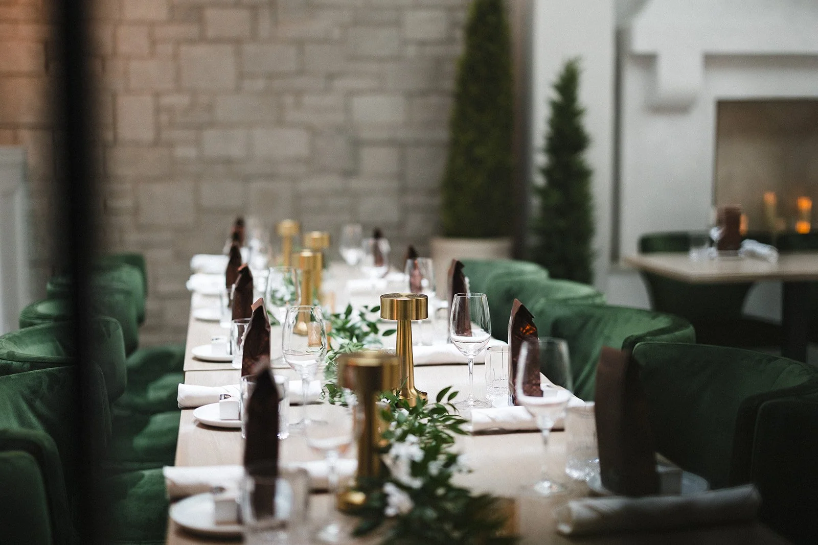 Lush green chairs flank a white table set with glasses, chocolates, gold lanters and white place settings.