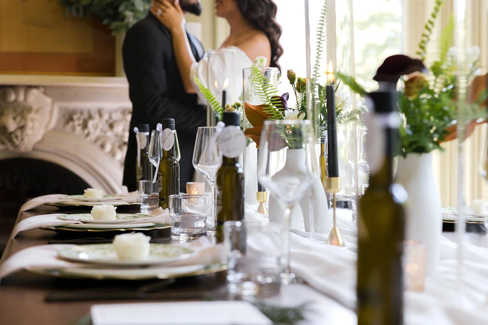 Newlyweds stand at the end of a beautifully dressed table and in front of a stone fireplace.