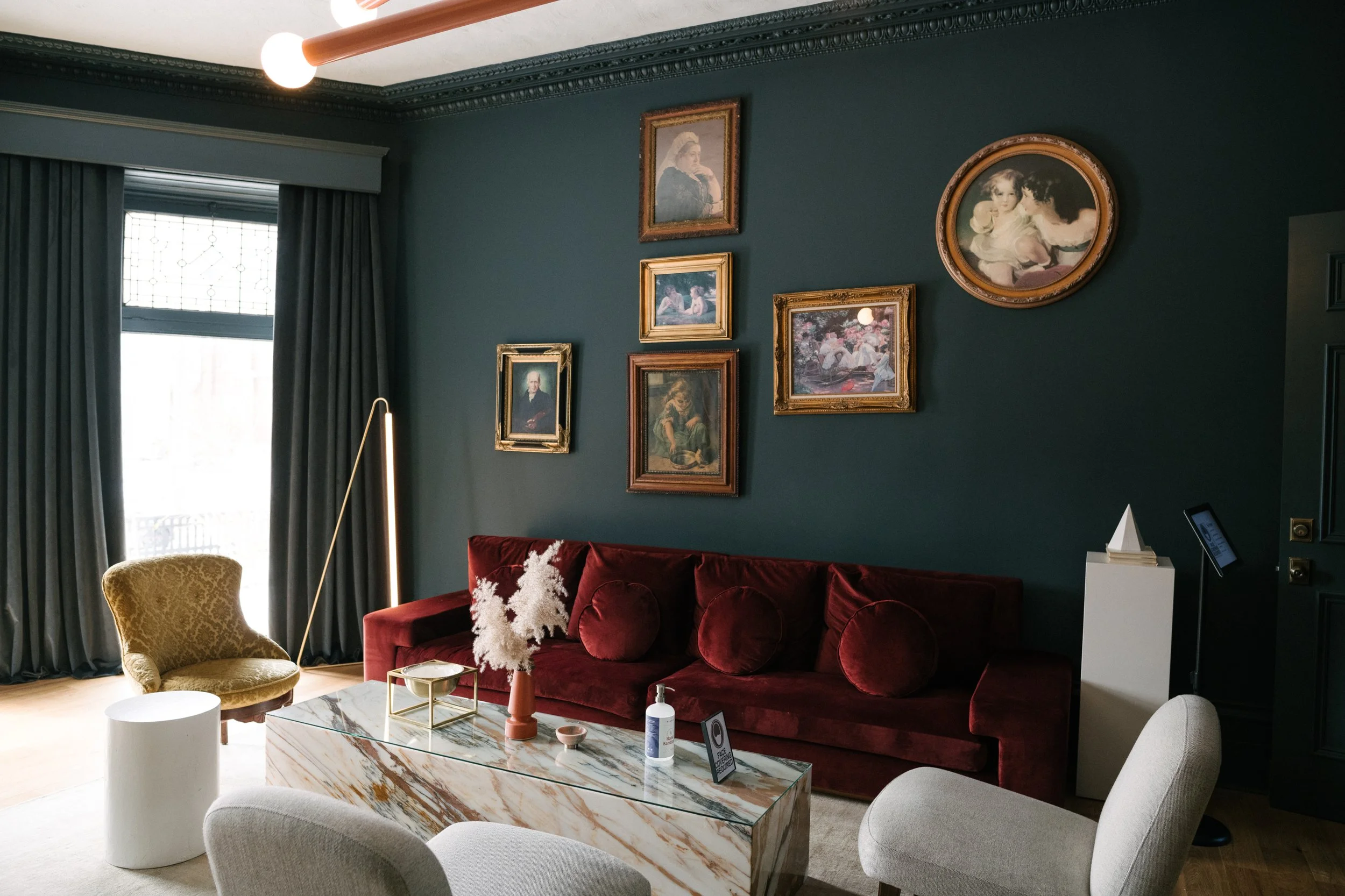 Burgundy Sofa in a room painted in deep greens with lush green drapes and a marble coffee table.