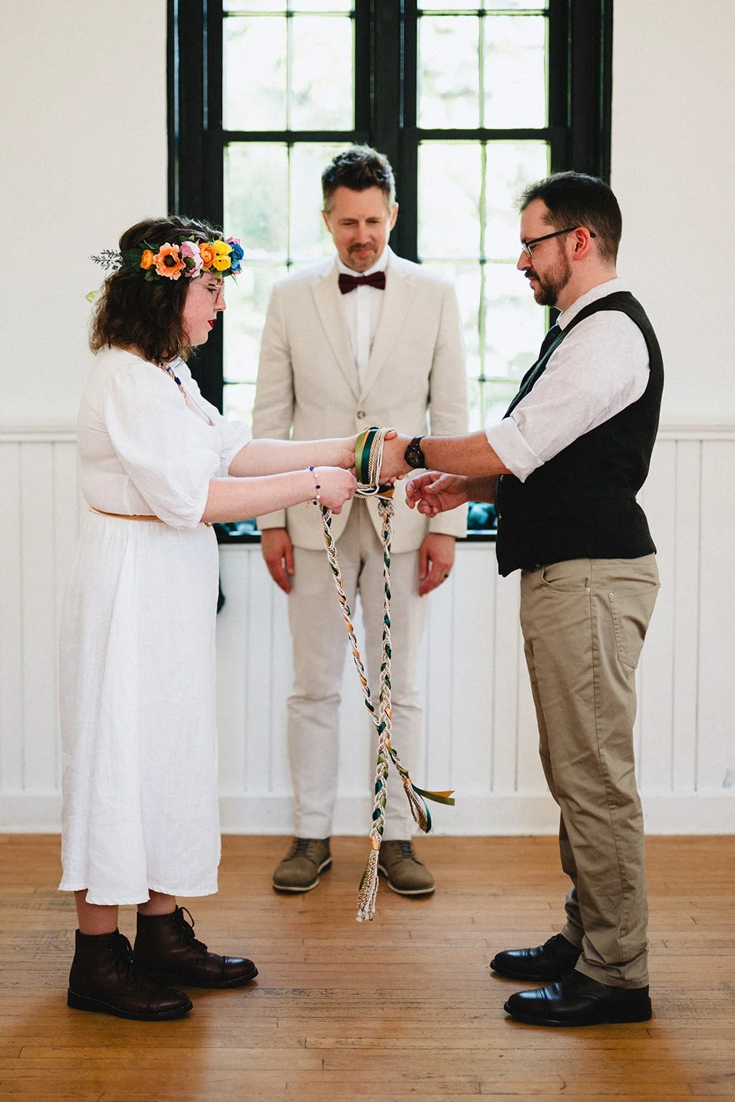 A couple exchanging wedding rings during a wedding ceremony, with an officiant standing behind them in front of a window.