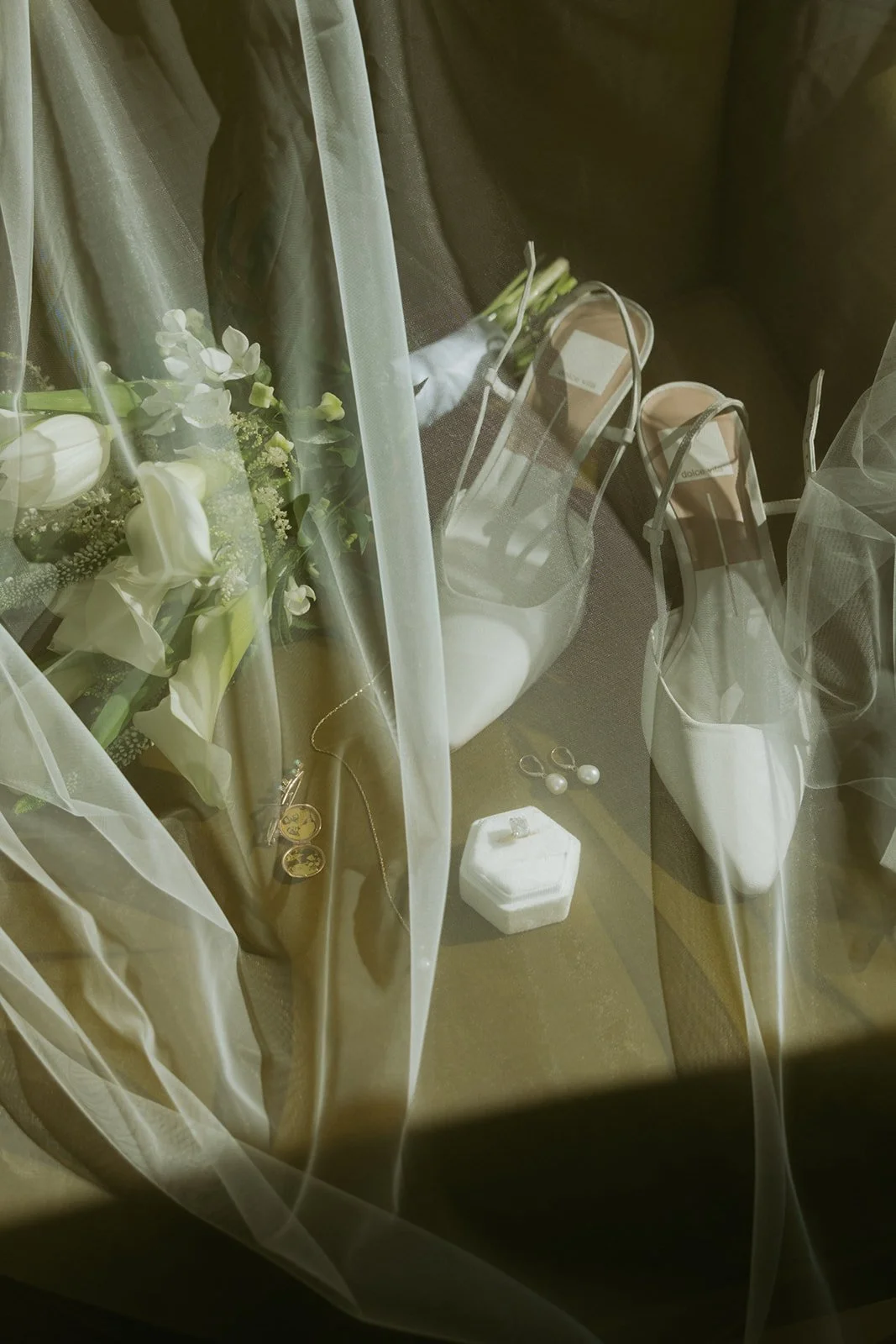 Wedding shoes, jewelry, flowers, and a ring box are visible behind a sheer curtain.