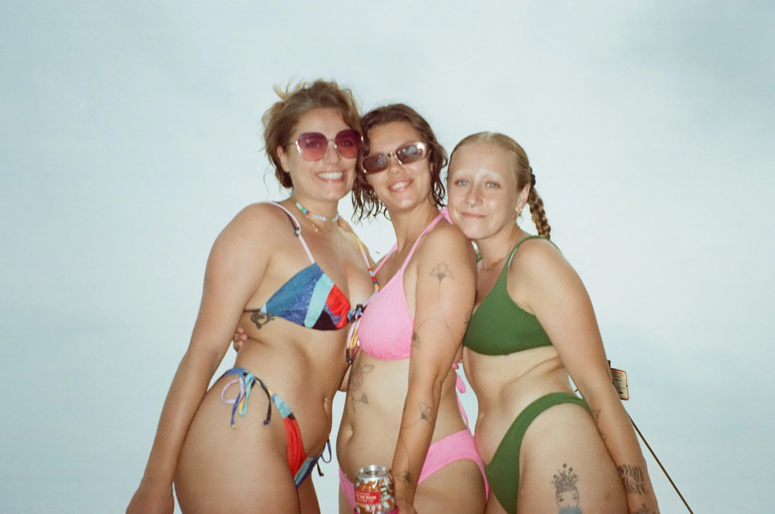Three women in bikinis smiling and posing together, standing against a plain white background.