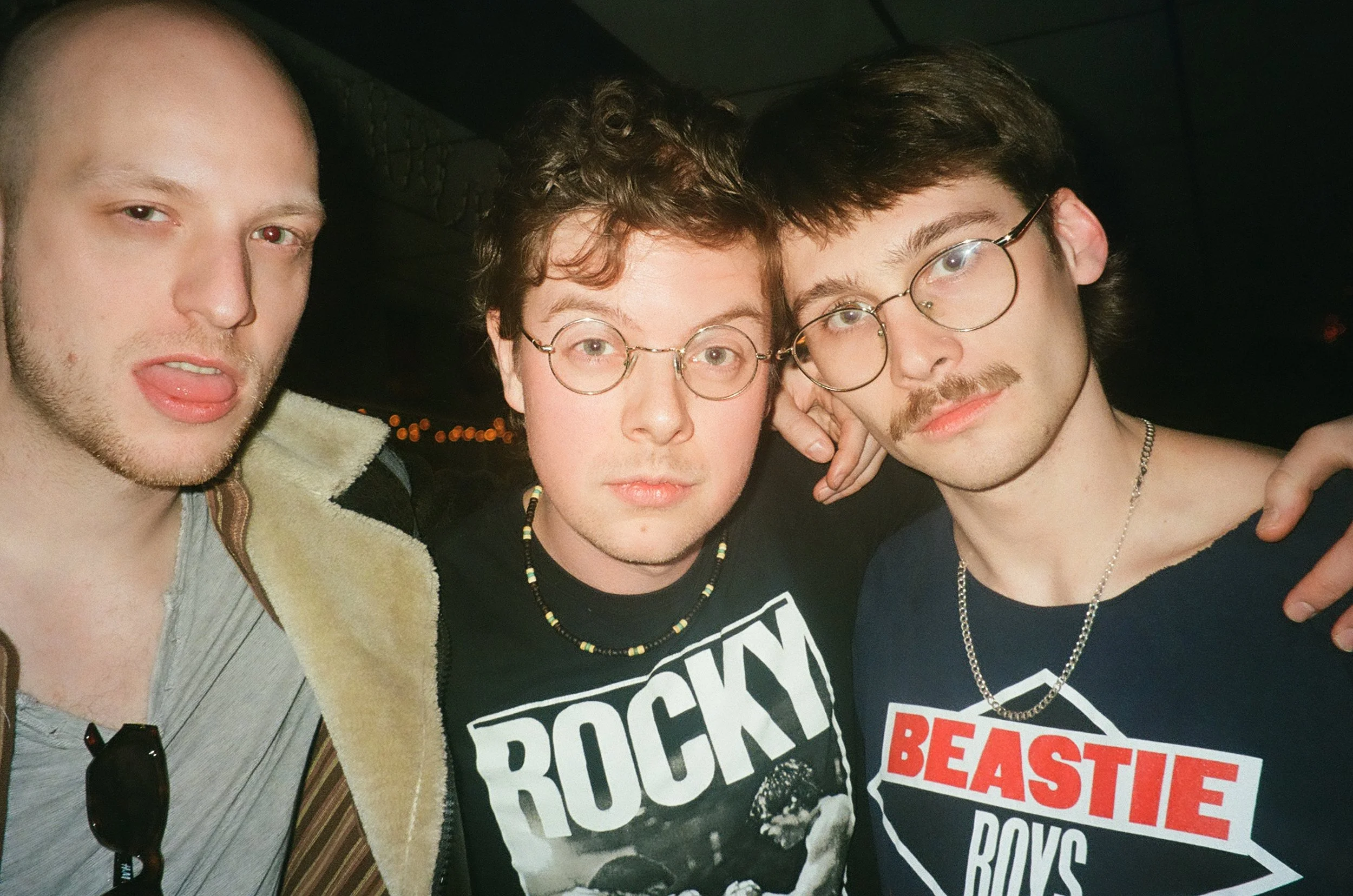 Three young men posing closely together for a selfie, with two of them wearing glasses and one sticking out his tongue.
