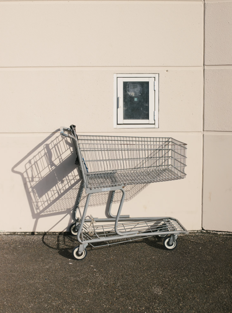 Empty shopping cart leaning against a beige wall with a small window.