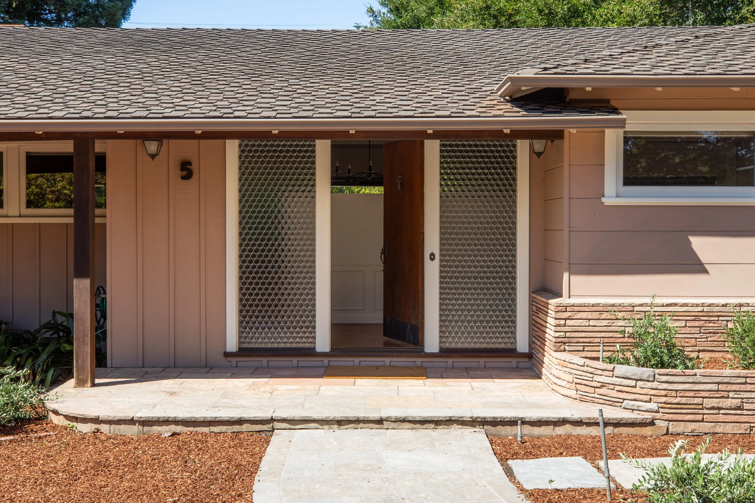 Front exterior of a house with a covered porch, brick steps, and garden area, featuring siding, windows, and a door.