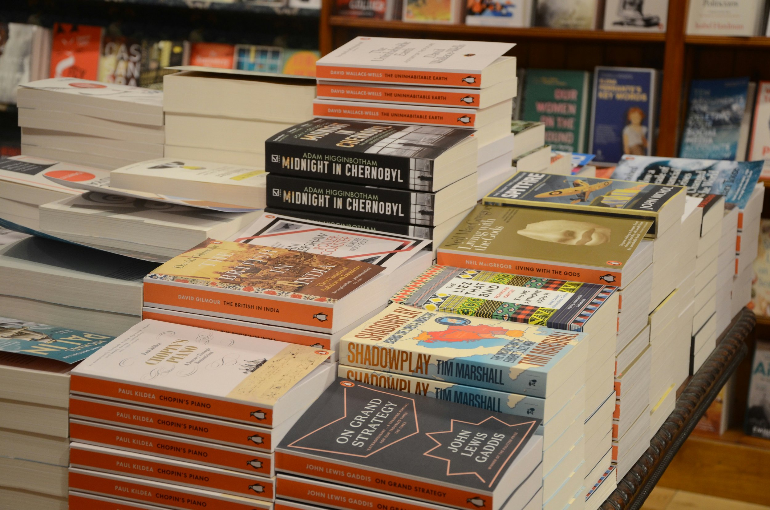 Stacks of books on a table at a bookstore, written by authors with a purpose using professional ghostwriting and editing support.  The background shows shelves filled with more books.