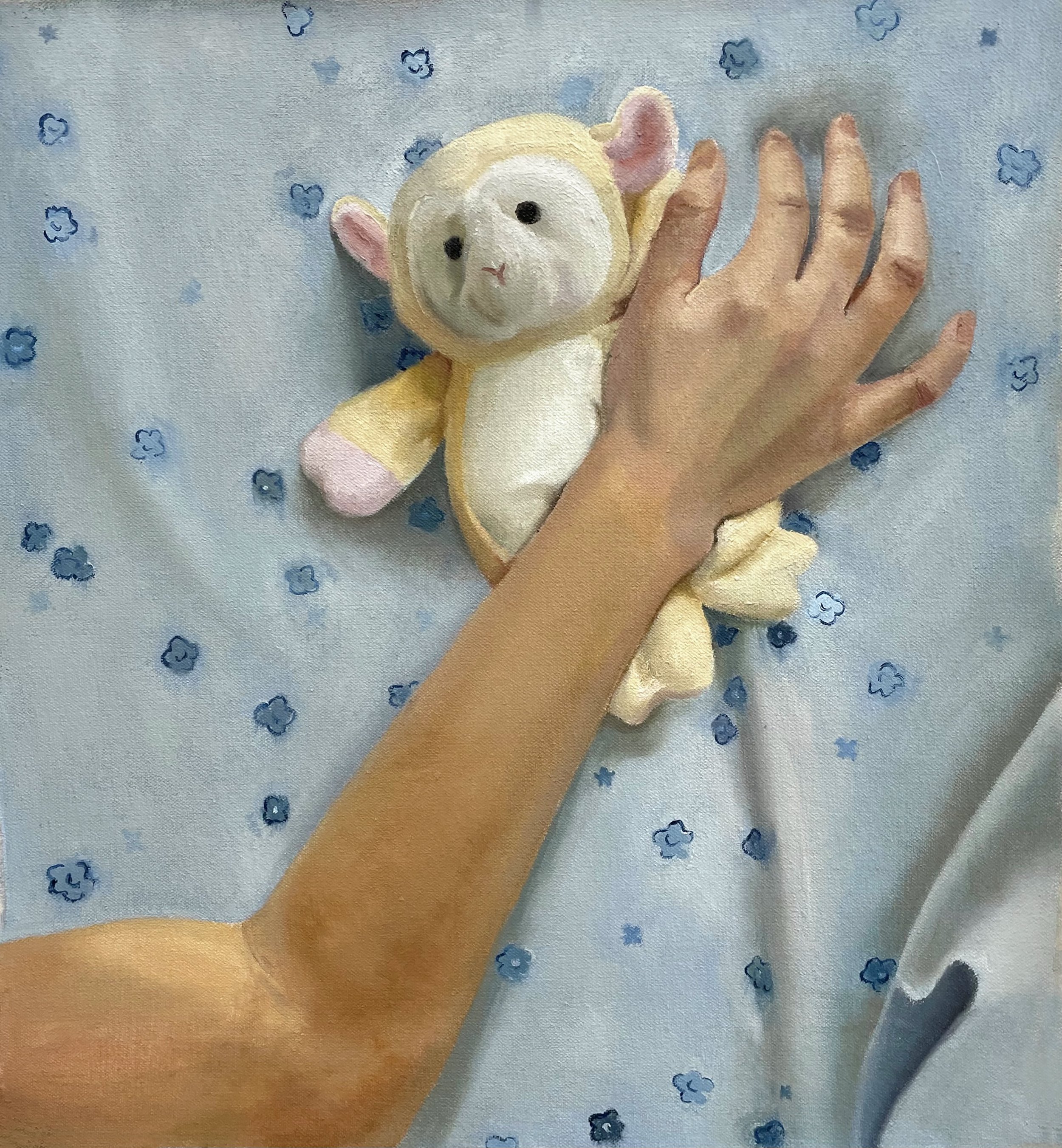 Hand holding a sheep plush on a blue fabric background with small blue flowers.