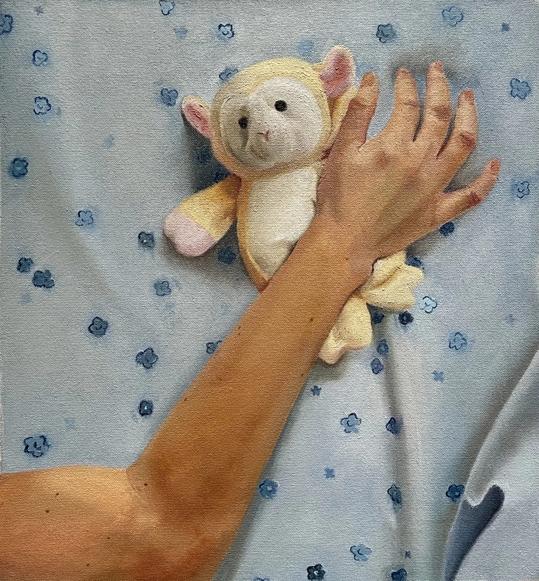 A person holding a small sheep plush on top of a sheet that's blue with flowers.