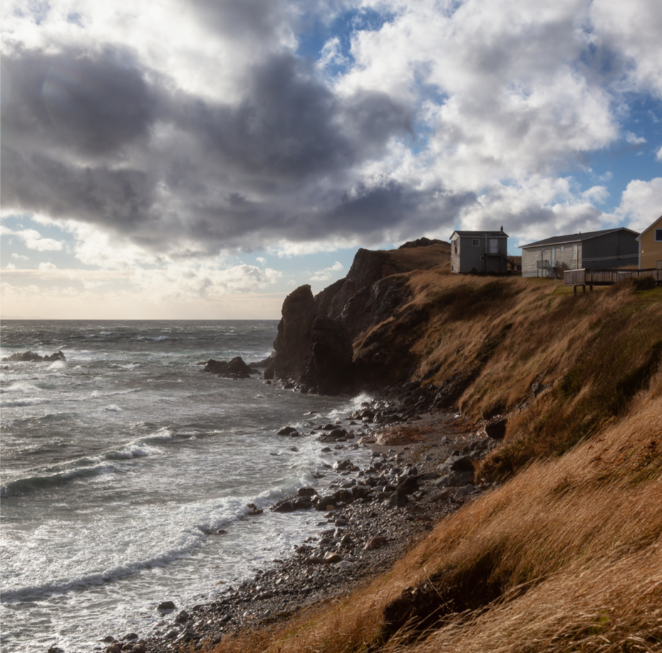 Cliffs overlooking the ocean with houses on top, rocky shoreline, and cloudy sky.