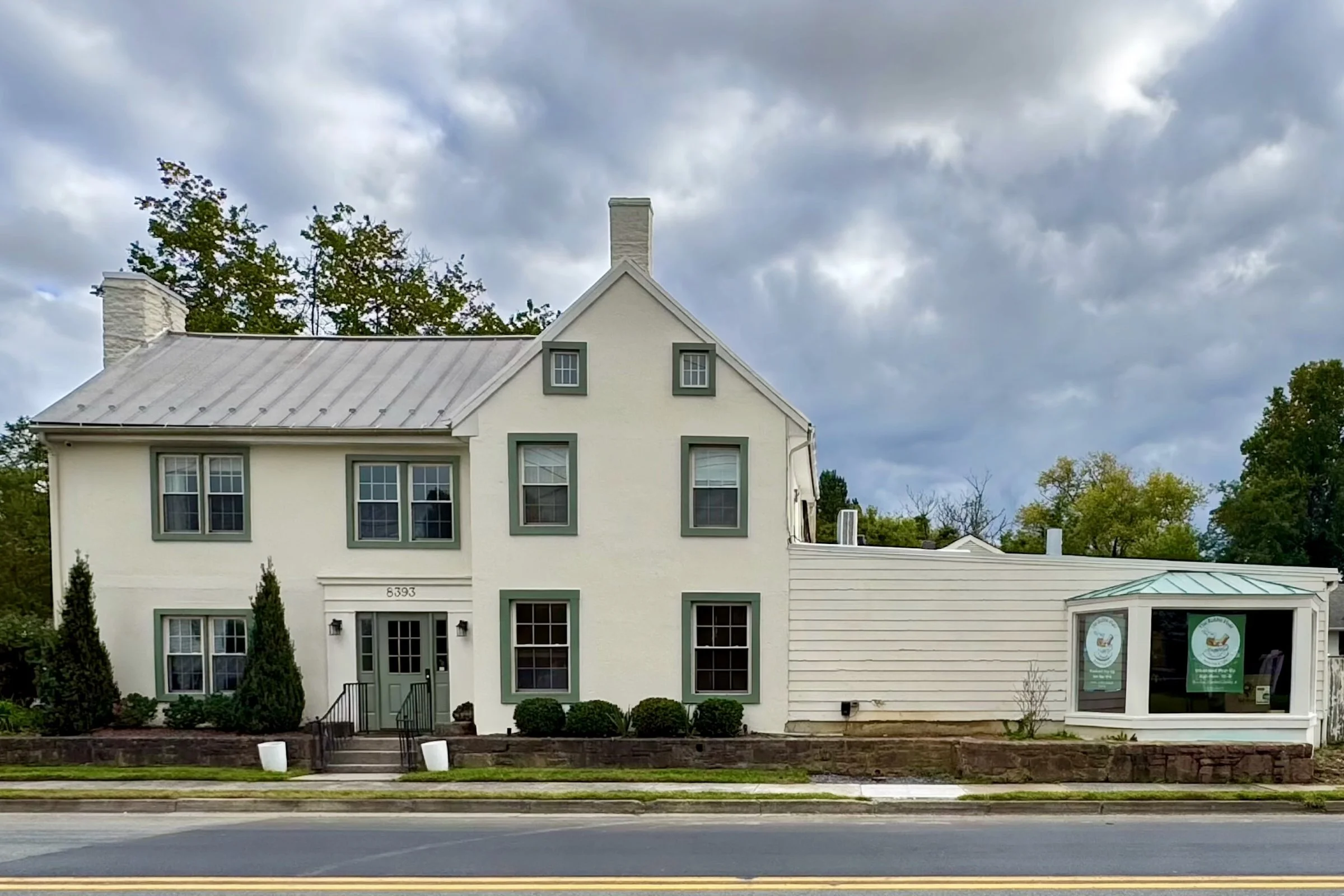 The Rabbit Hole from West Main Street: a cream two-story building with green trim behind a low stone wall, and the shop's glass bay to the right.