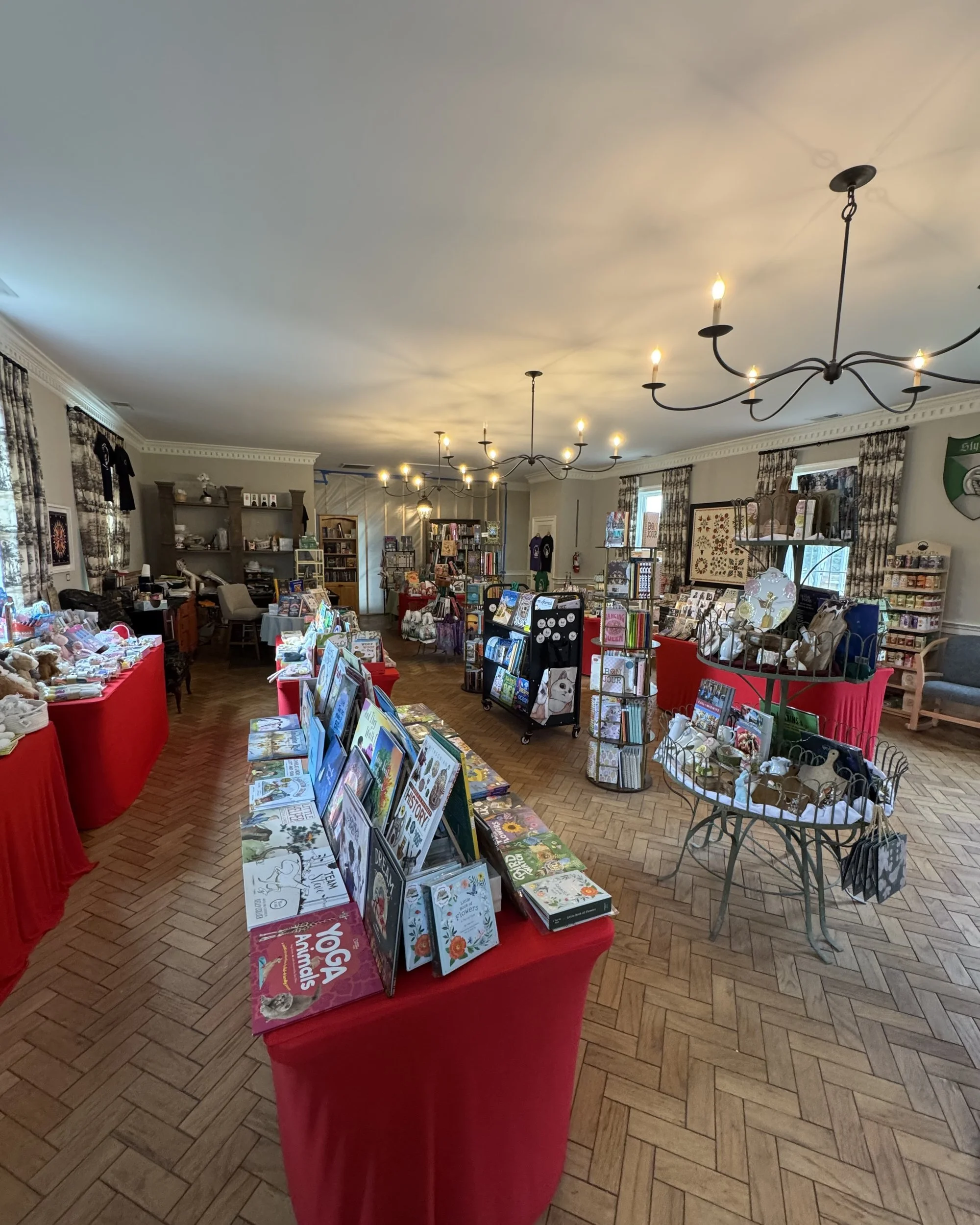Inside the shop: red-draped tables of picture books and gifts under iron candle chandeliers, on a herringbone wood floor.