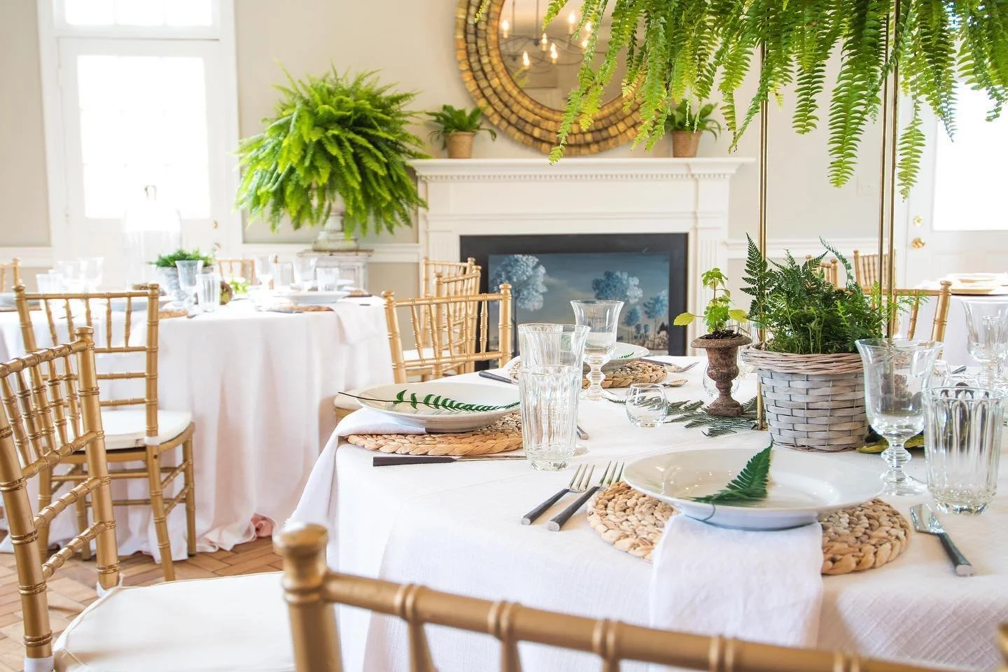 The Drawing Room set for dinner: round tables, ferns, and gold chairs by the fireplace.