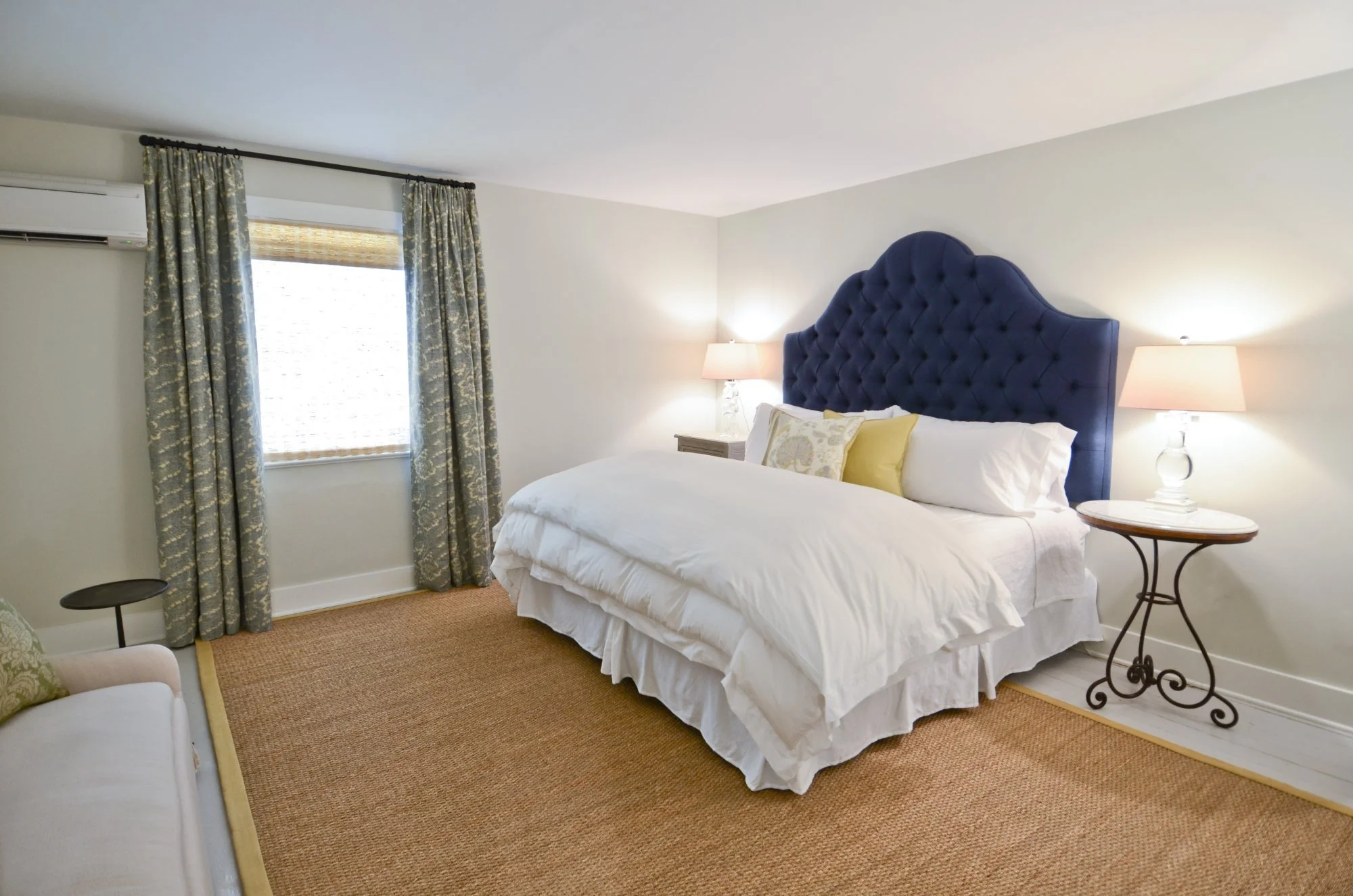 The Clover: a king bed with a navy tufted headboard beside a window with green drapes.