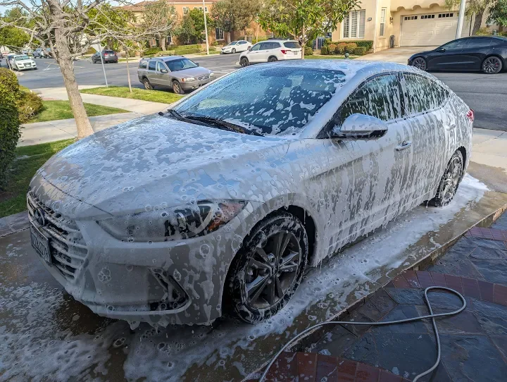 A silver sedan car being washed with soap and water on the driveway.