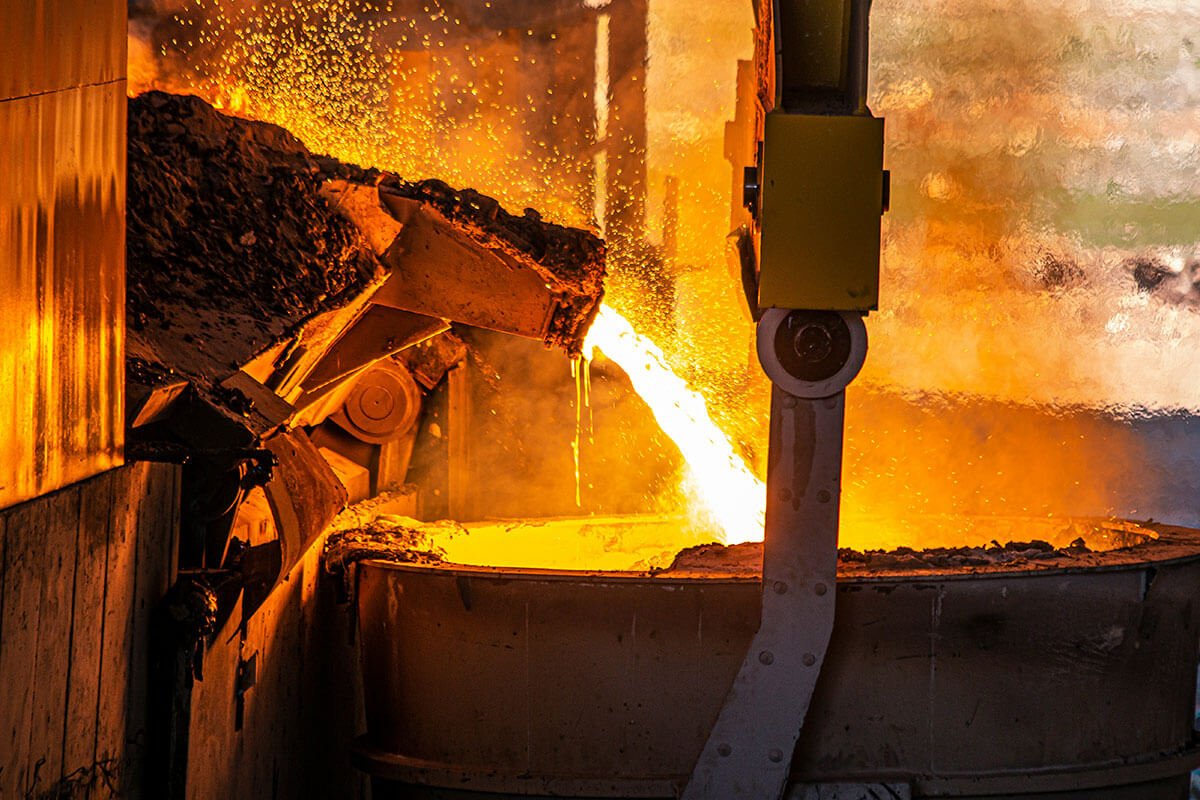 Un horno de fundición con metal fundido en proceso de vertido, altas temperaturas y chispas en un entorno industrial.