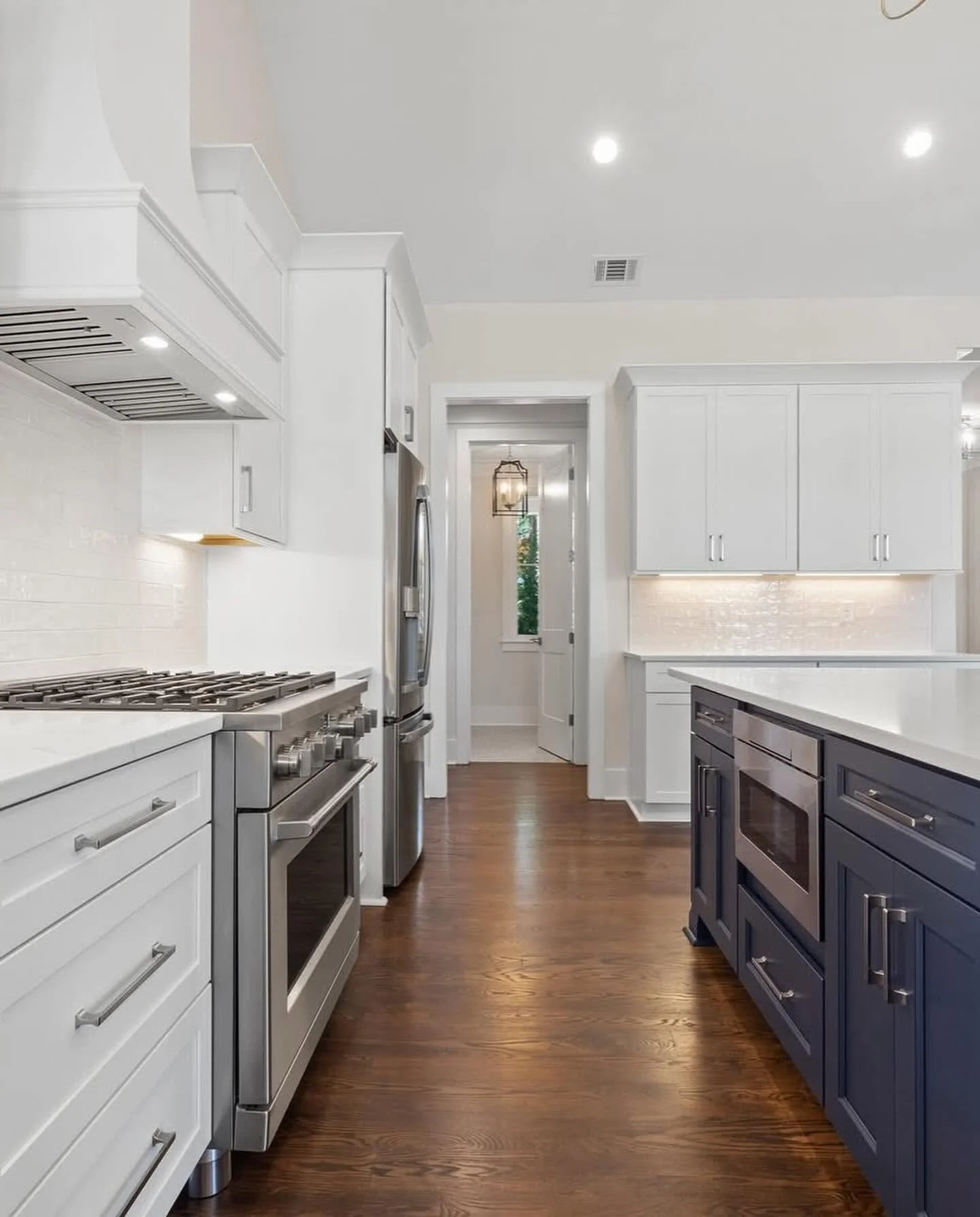 Modern kitchen with white upper and lower cabinets, a navy island, stainless steel appliances, and hardwood floors.