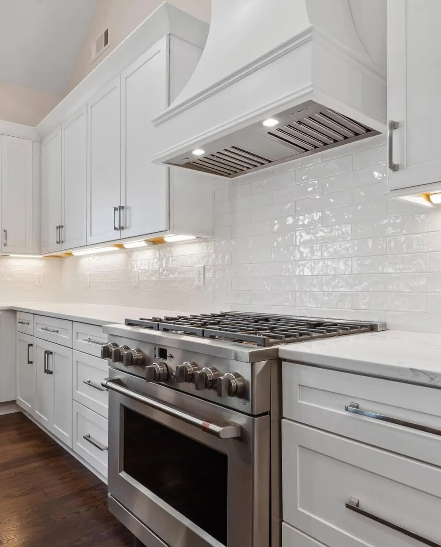 Clean white kitchen with stainless steel stove and white cabinets, white tile backsplash, and dark hardwood floor.