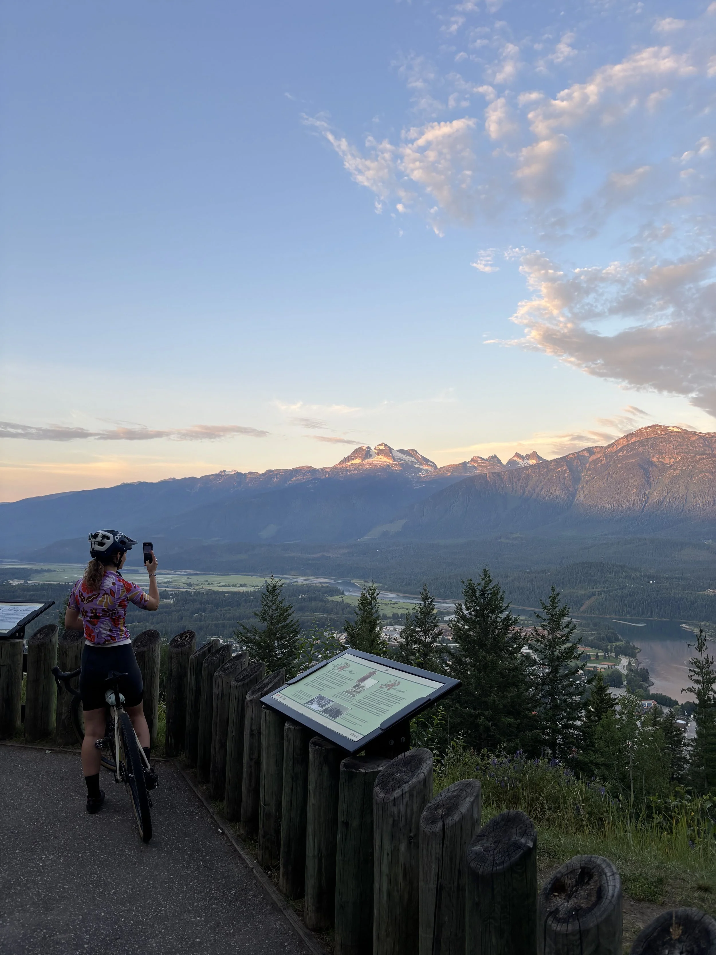A female cyclists pauses at a lookout to take a photo of Revelstoke and the Selkirk mountain range