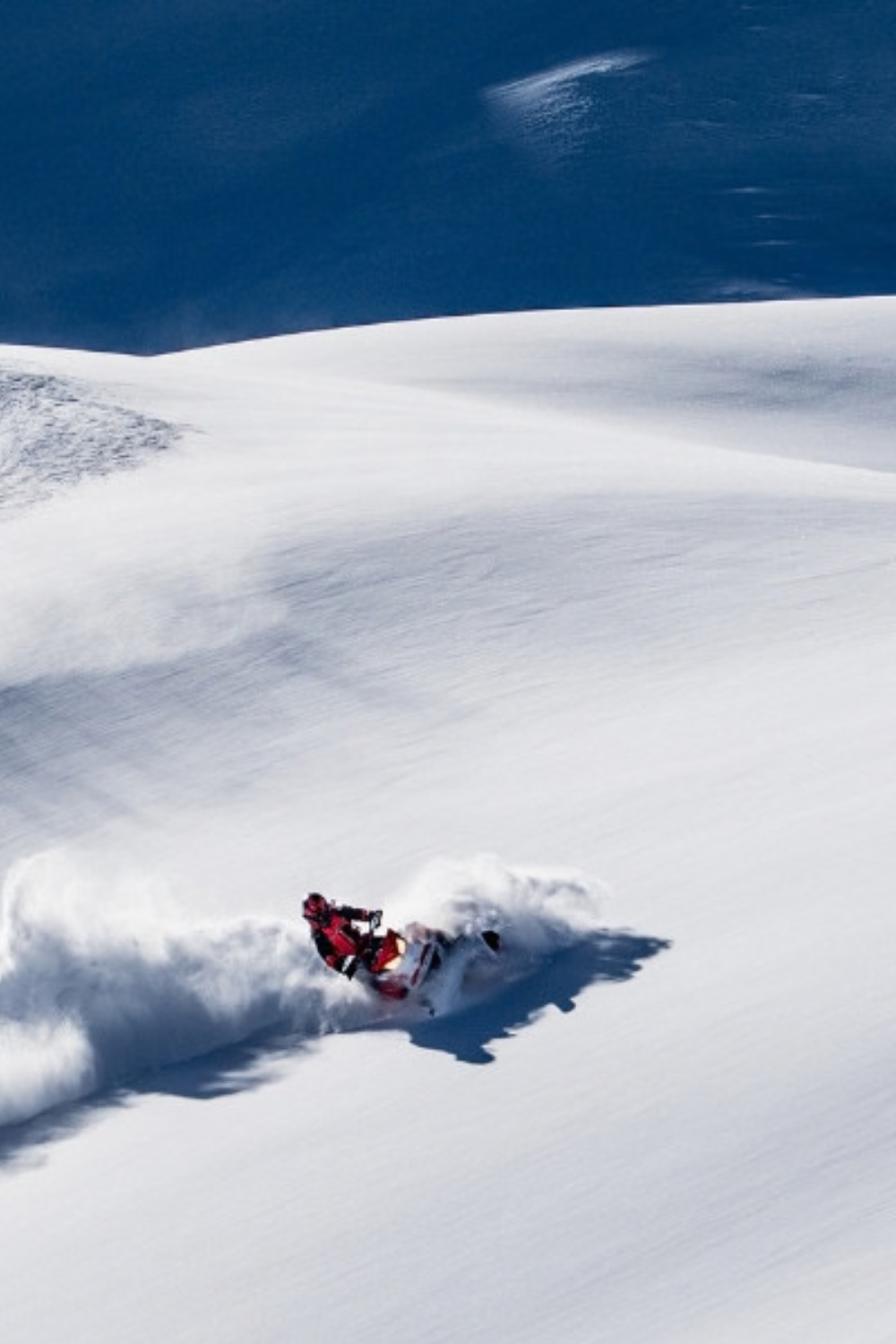 A person in winter gear snowboarding down a snow-covered mountain slope in a remote, snowy landscape.