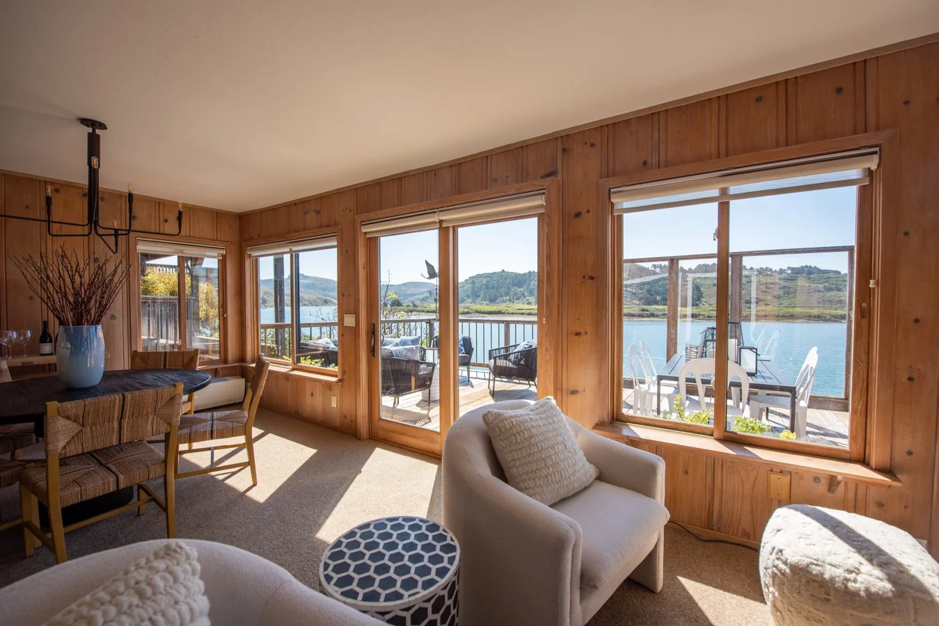Living room with large windows overlooking a lake, with a view of the deck and outdoor furniture.