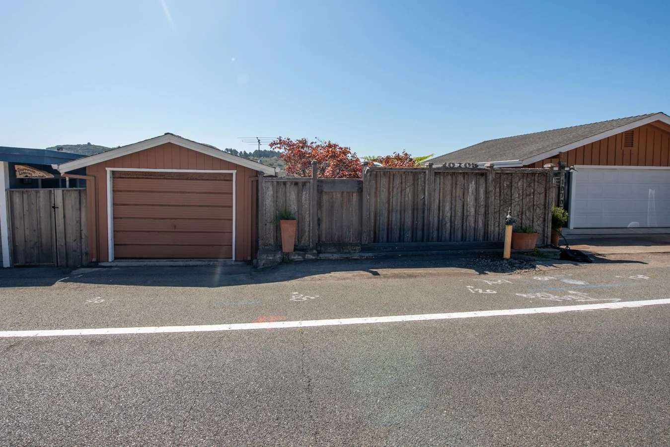 A view of a residential area with two garages separated by a wooden fence, with potted plants and a clear blue sky.