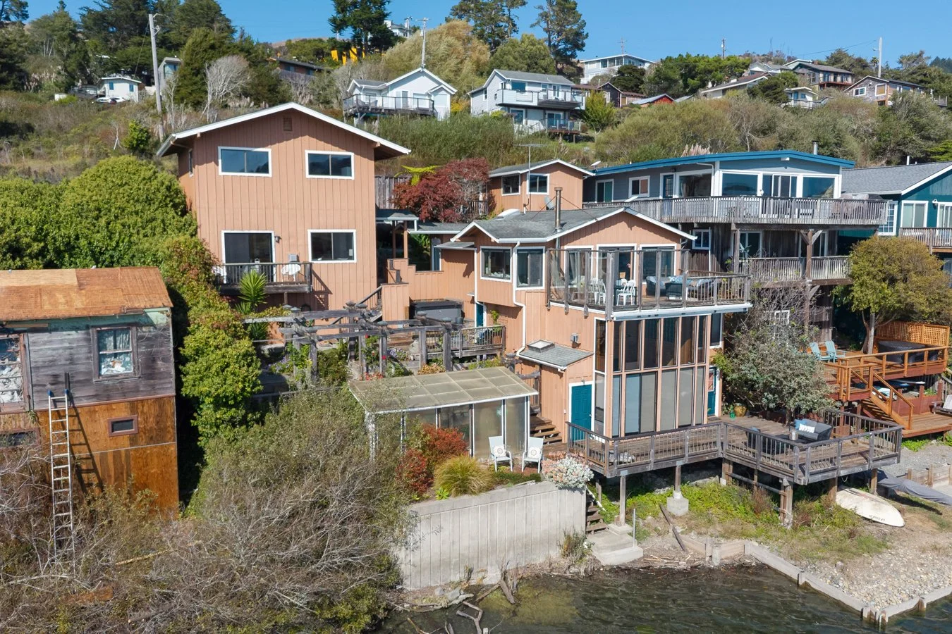 Aerial view of multiple houses on a hillside near a body of water, with trees and greenery around.