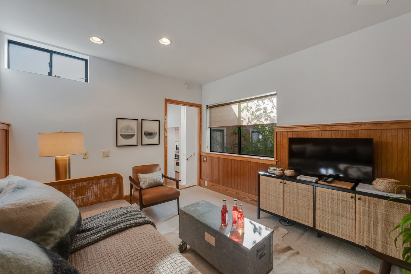 Living room with a bed, armchair, TV, and decorative wall art, featuring natural wood accents and large windows.