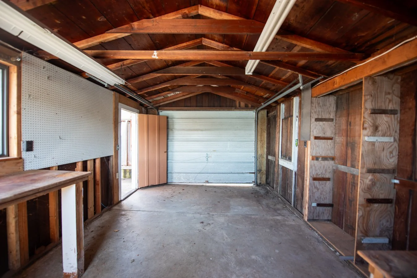 Empty garage with wooden walls, fluorescent lighting, a concrete floor, and a metal garage door.
