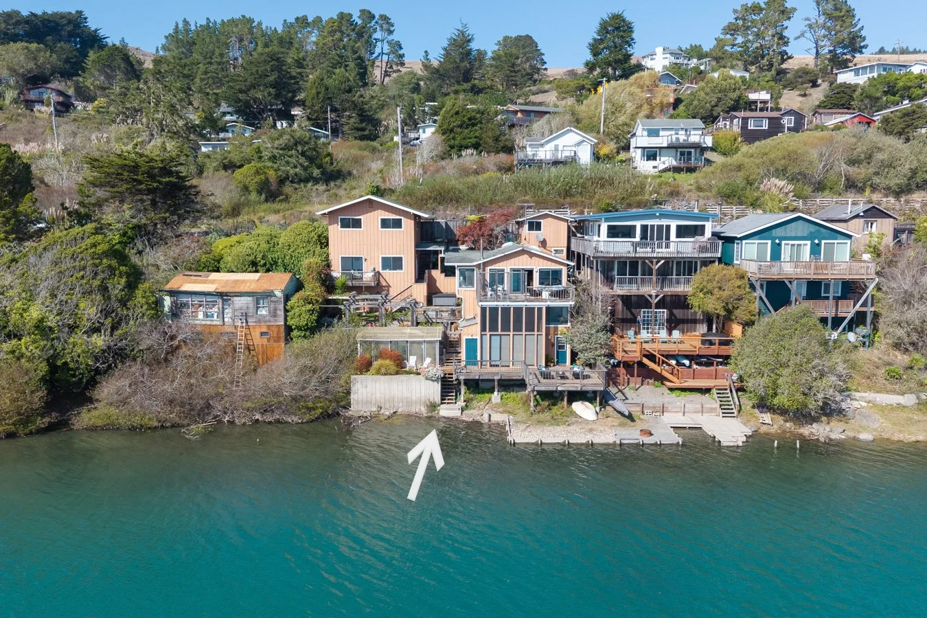 Houses on a hillside near water, with stairs and docks leading to the shoreline, and trees surrounding the area.