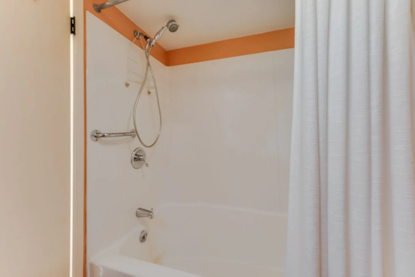 Bathroom shower with a white curtain, orange border at the top, and a showerhead with a hose and mixer.