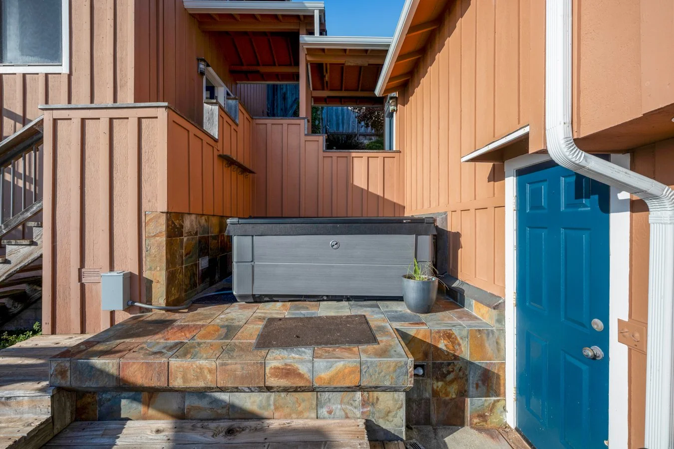 Backyard with wooden fencing, hot tub, potted plant, blue door, and drainage pipes.