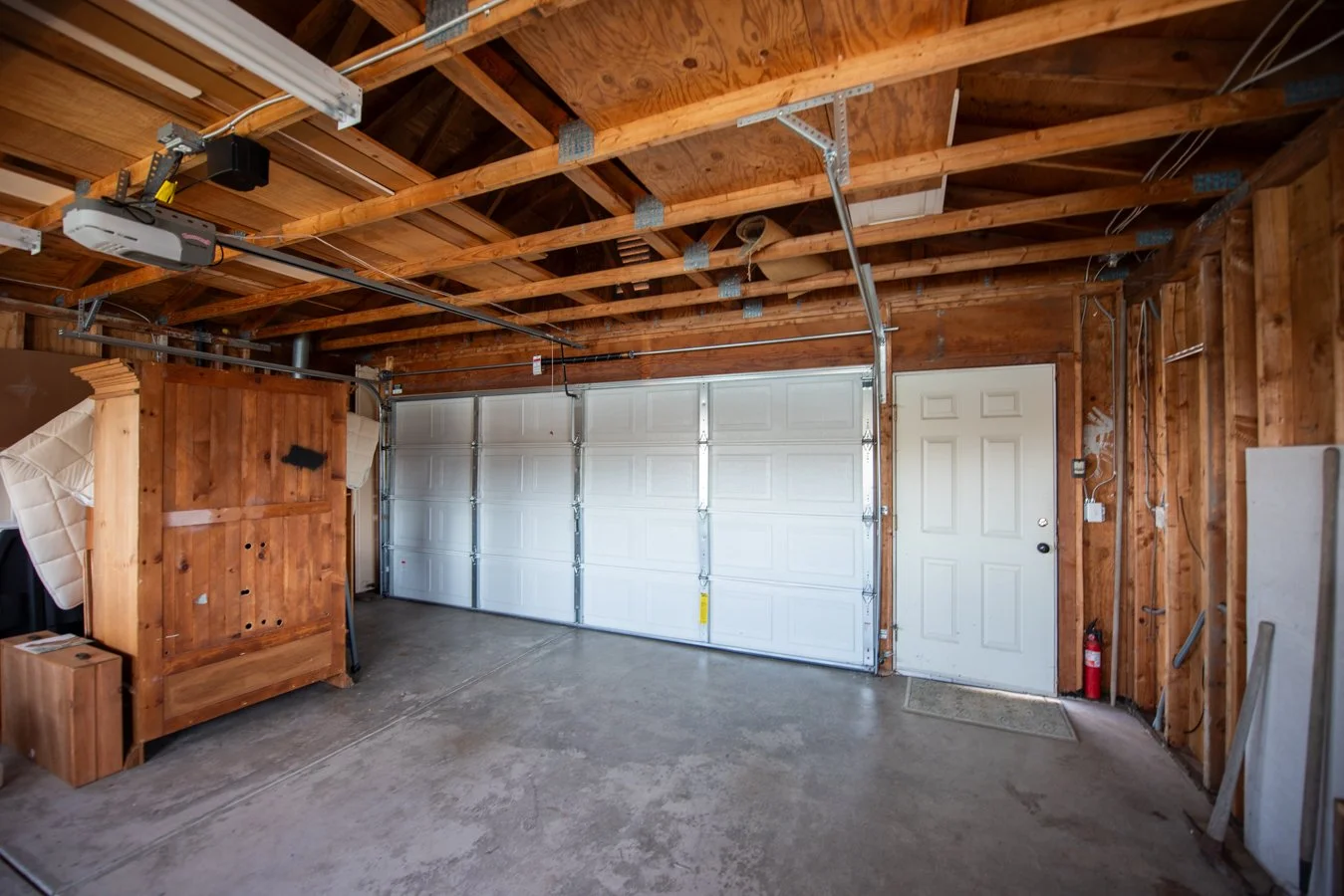 Empty garage with wooden frame, concrete floor, white garage door, and basic utility setup.