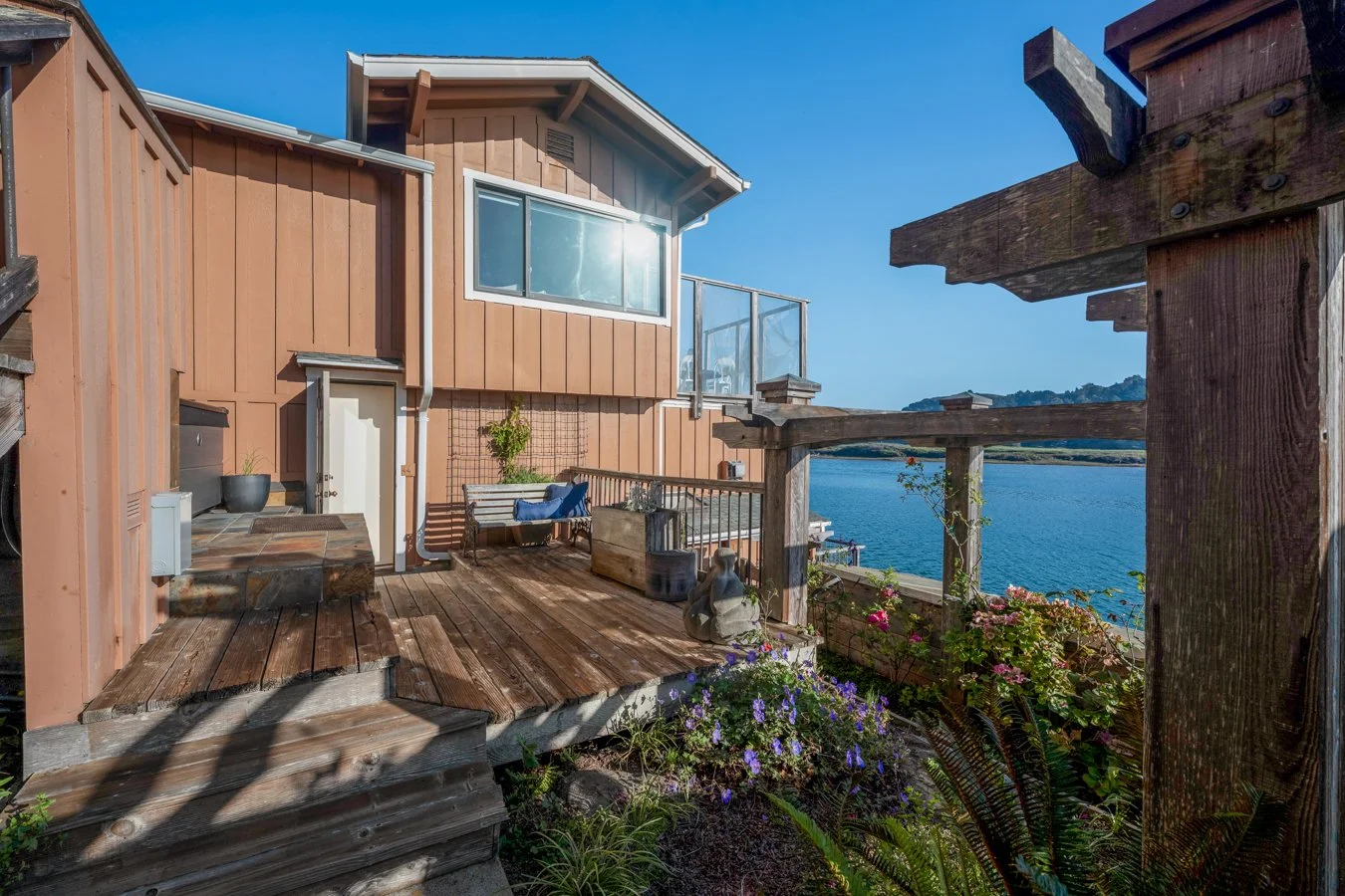 Beach house balcony overlooking the water with a wooden deck, flower pots, and garden decorations.