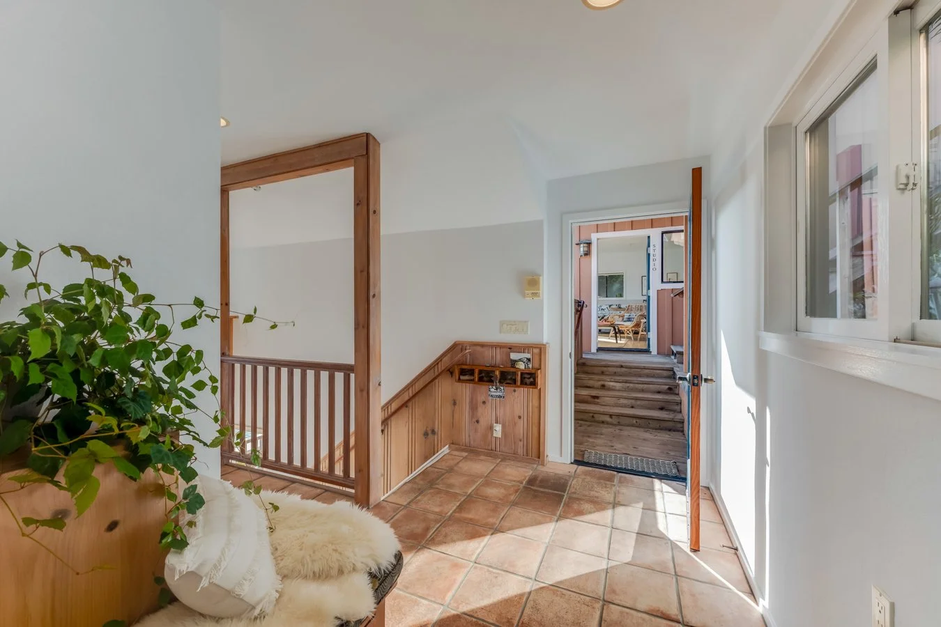 Entryway with terracotta tile floor, open door leading outside to a porch, wooden staircase, and a window on the right.