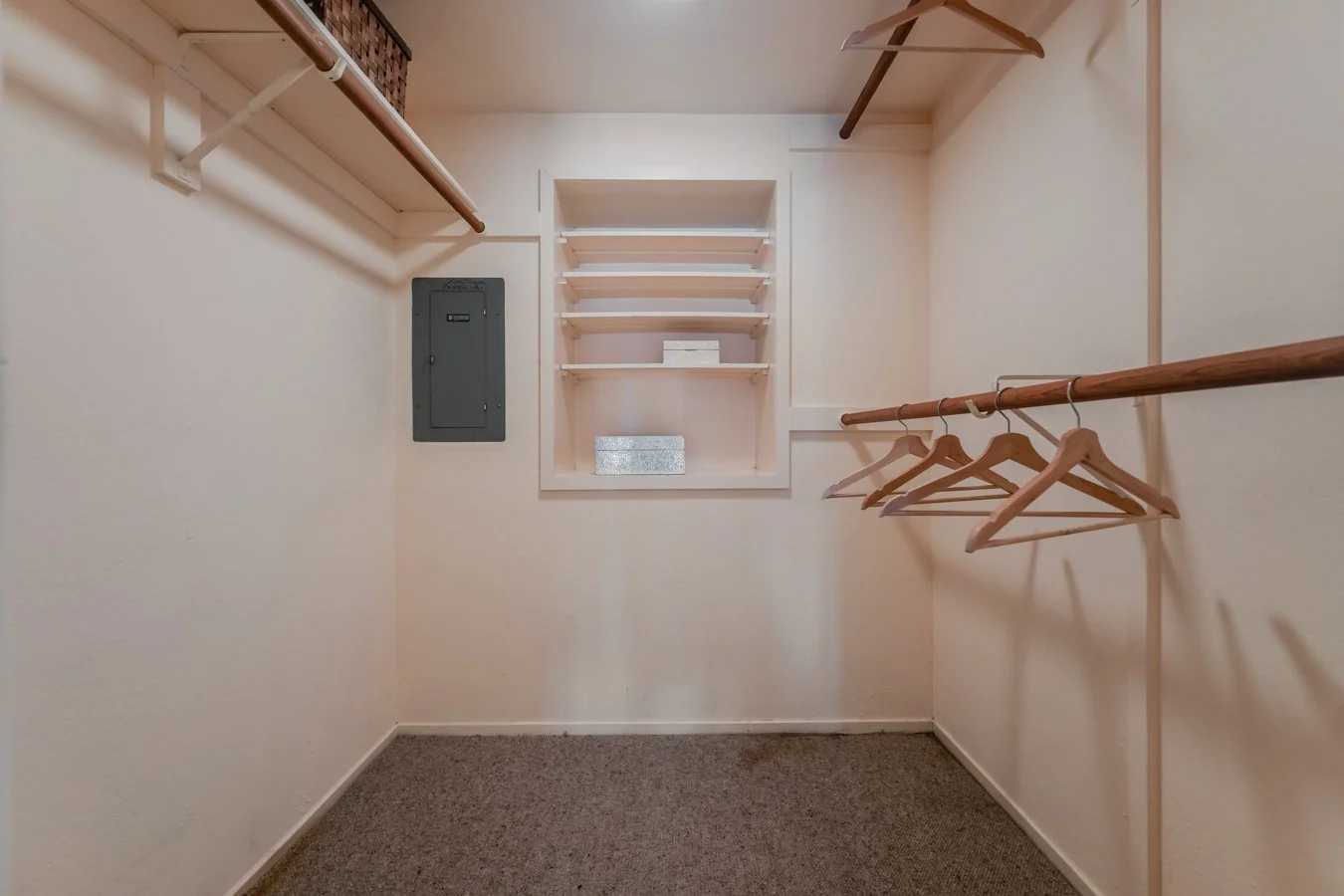 Empty walk-in closet with hanging rods, a small shelf, and an electrical panel.