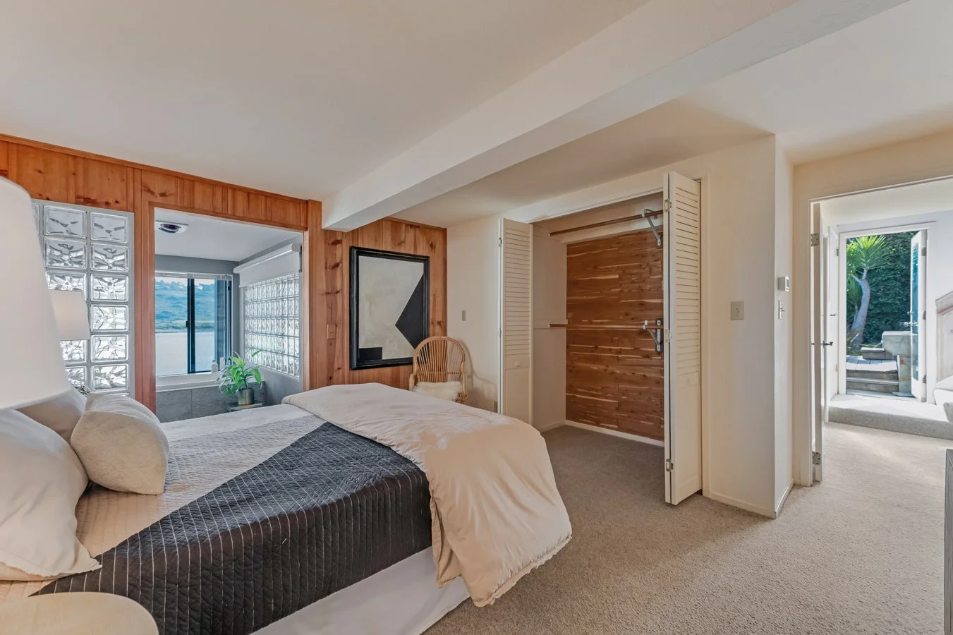 A bedroom with a bed, a window with a view of water, and an open door leading outside to a patio.