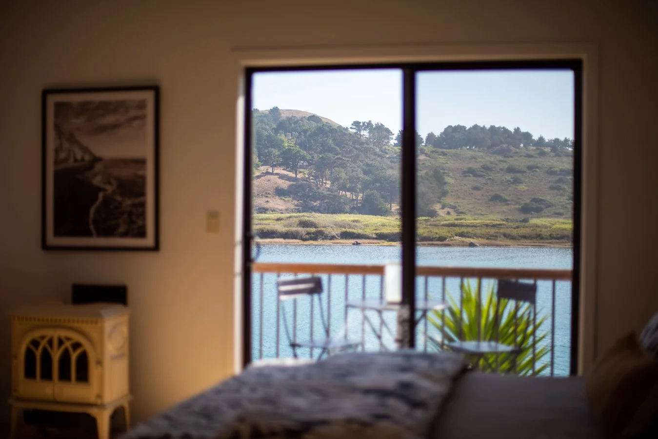 Looking out from inside a bedroom through a sliding glass door to a patio with a view of a river, trees, and hills in the distance.