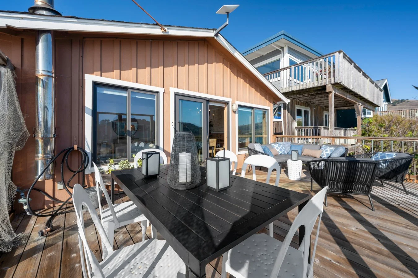 Outdoor wooden deck with dining table, chairs, and lounge seating under a clear blue sky.