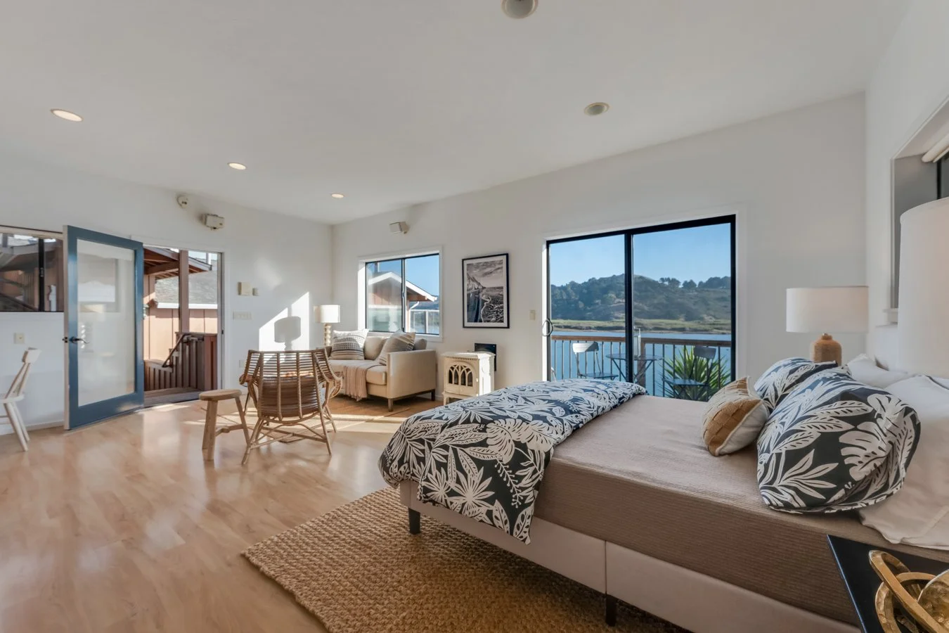 Bright living room with a bed, sofa, dining table, and large windows showing a scenic water view.