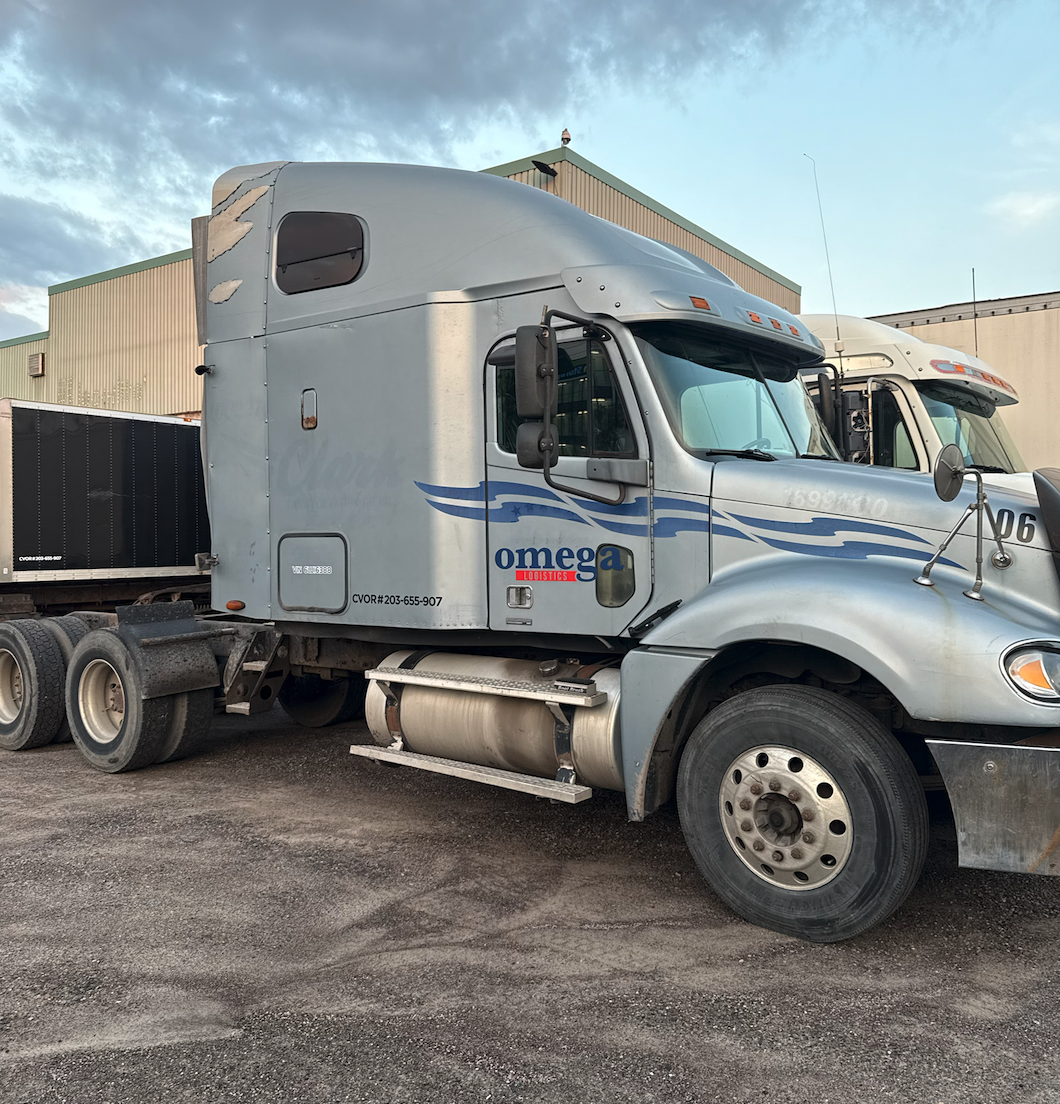 A silver semi-truck parked outdoors in front of industrial buildings during daytime.