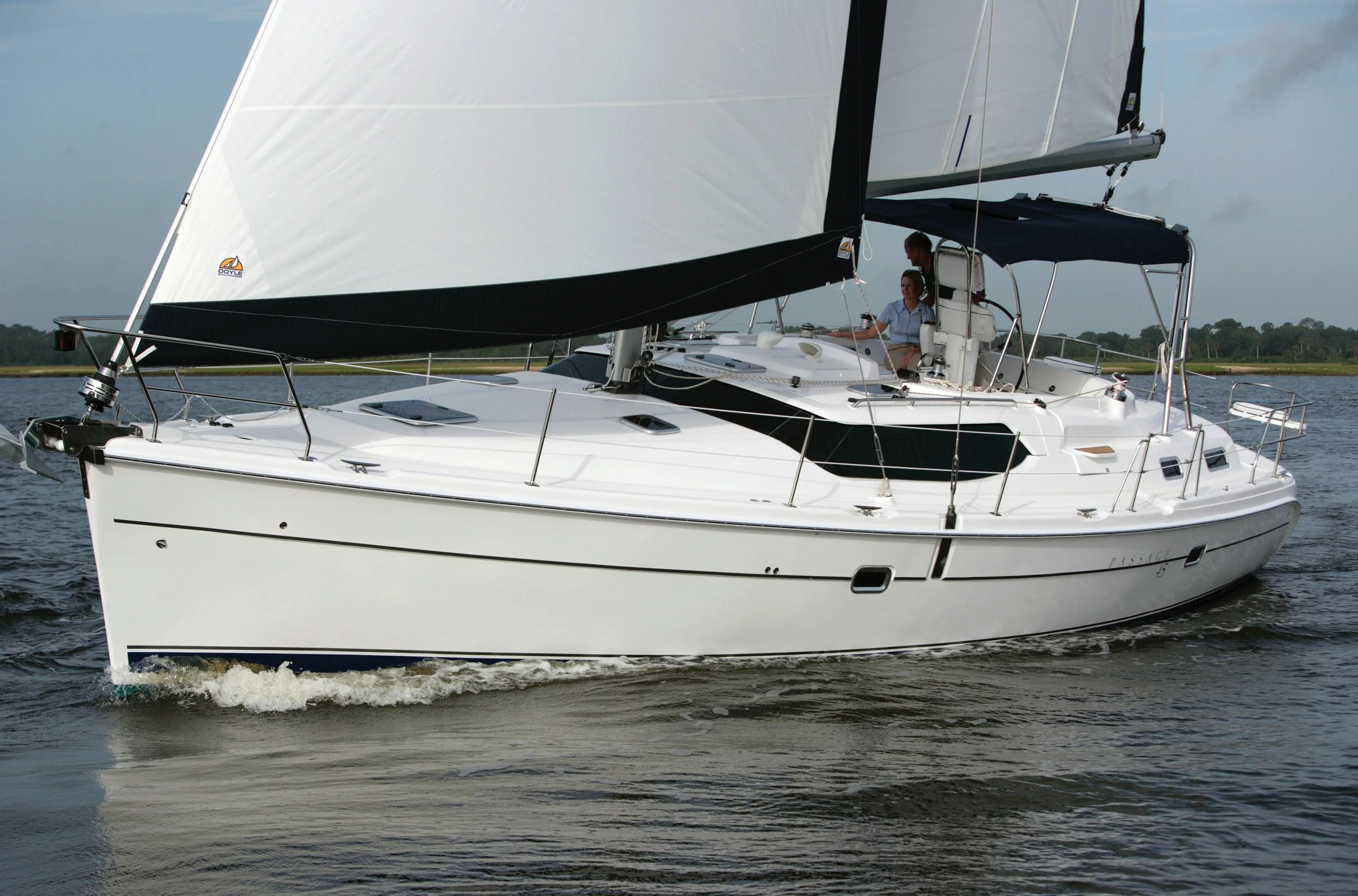 A white sailboat with a black sail on a body of water, with two people on deck controlling the boat.